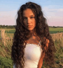 a woman with long curly hair is standing in a field