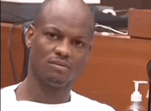 a bald man in a white shirt is sitting in front of a hand sanitizer dispenser .