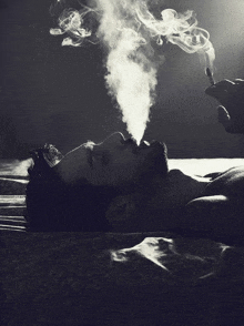 a man with a beard is laying on a bed smoking a cigarette