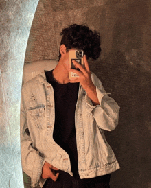 a man in a denim jacket is taking a picture of himself in the mirror