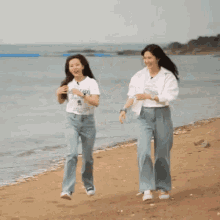 two women are dancing on a beach with one wearing a shirt that says ' i love you ' on it