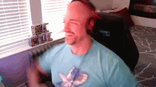 a man wearing headphones and a blue shirt with a butterfly on it sits in a gaming chair