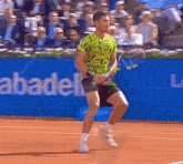 a man in a green shirt is holding a tennis racquet on a tennis court in front of a sign that says abadel