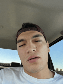 a man wearing a white shirt and a hat is sitting in a car with his eyes closed