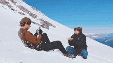 two people are sitting on a snowy mountain and one of them is looking at his phone