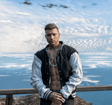 a shirtless man with a tattoo on his chest stands in front of the ocean