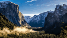 a valley surrounded by mountains with trees and clouds