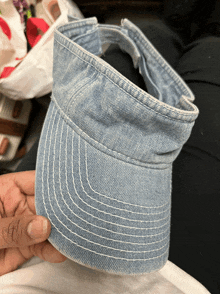 a person holding a light blue denim visor in their hand