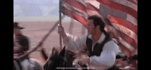 a man is riding a horse and holding an american flag in front of a crowd of people .