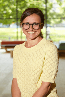 a woman wearing glasses and a yellow shirt smiles