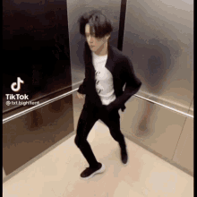 a man in a suit and white shirt is dancing in an elevator with tiktok written on the bottom