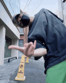 a man wearing a black mask stands next to a no parking cone