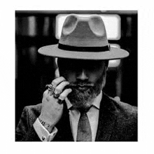 a man with a beard wearing a fedora hat and smoking a cigar .