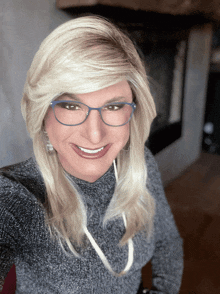 a blonde woman wearing glasses and a grey sweater smiles for the camera