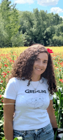 a woman wearing a gremlins t-shirt smiles in front of a field of flowers