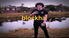 a young man wearing a black shirt that says blockha stands in front of a body of water