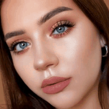 a close up of a woman 's face with blue eyes and a pink lip color .