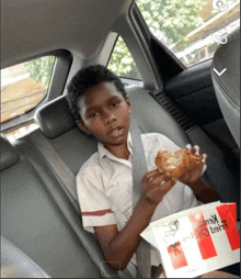 a young boy is sitting in the back seat of a car eating a kfc chicken sandwich