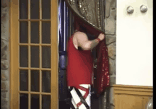 a man in a red tank top is standing in a doorway holding a red cloth .