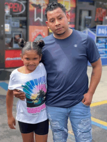 a man in a champion shirt stands next to a little girl wearing a shirt that says sunset state