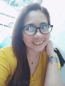 a woman wearing glasses and a yellow shirt smiles for the camera .