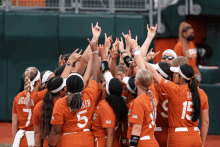 a group of female softball players huddle together with their arms in the air