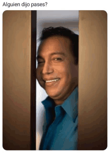 a man in a blue shirt is peeking through a doorway and smiling .