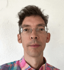 a man wearing glasses and a colorful plaid shirt is looking at the camera .