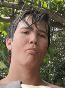 a young man with wet hair is making a funny face while standing under a tree .