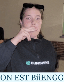 a woman wearing a black sunshine shirt covering her mouth with her hand