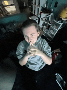 a young girl is sitting in a dark room with her hands folded