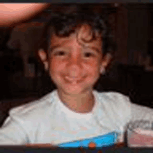 a young boy is smiling for the camera while sitting at a table in a restaurant .