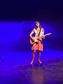 a woman in a red polka dot dress is playing a guitar on a stage