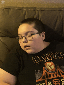 a boy wearing glasses and a shirt that says giants is sleeping on a couch