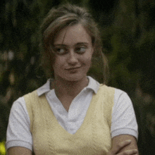 a girl wearing a yellow vest and a white shirt looks at the camera