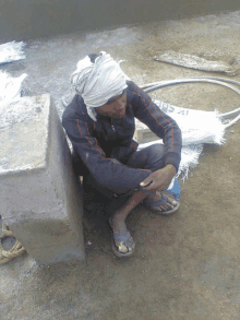 a man wearing a bandana sits on the ground next to a bag that says ' i 'm sorry '