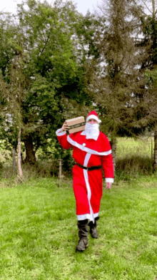 a man dressed as santa claus is carrying a box in a field