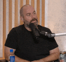 a man with a beard is sitting in front of a microphone with a bottle of water in front of him .