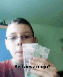 a boy with glasses is holding two bills in front of his face with the words " bedziesz moja " written on the bottom