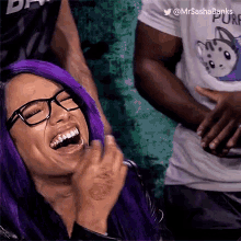 a woman with purple hair and glasses is laughing and clapping .