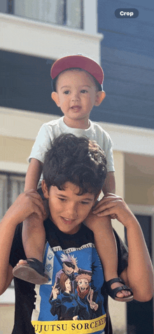 a boy wearing a jujutsu sorcerer shirt is carrying a little boy on his shoulders