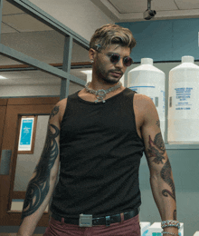 a man wearing sunglasses and a black tank top stands in front of a shelf with bottles of liquid soap on it