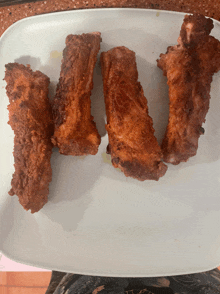 four fried pork ribs on a white plate on a counter