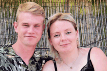 a man and a woman pose for a picture in front of a bamboo fence