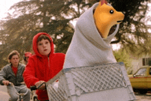 a boy in a red jacket is riding a bike with a stuffed animal wrapped in a blanket