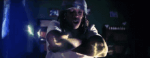 a man with dreadlocks is wearing a hat and a white shirt and is dancing in a dark room .