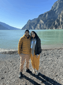 a man and a woman are posing for a picture in front of a body of water