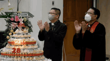 two men wearing face masks stand in front of a cake that says 28 on it