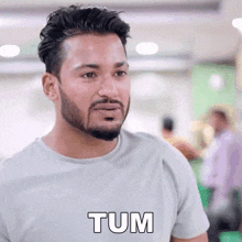 a man with a beard is wearing a white t-shirt and says tum