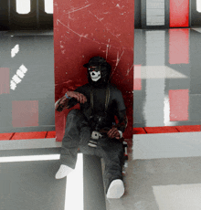 a man wearing a skull mask sits in front of a wall